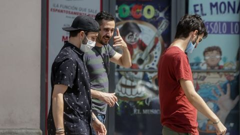Tres hombres pasean por Madrid, uno de ellos sin mascarilla.