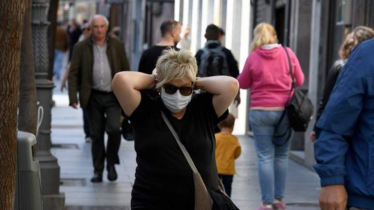 Una mujer se coloca la mascarilla mientras pasea por la calle.