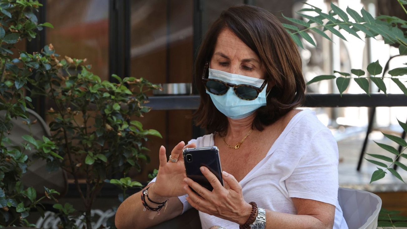 Una mujer mira el móvil con la mascarilla puesta.