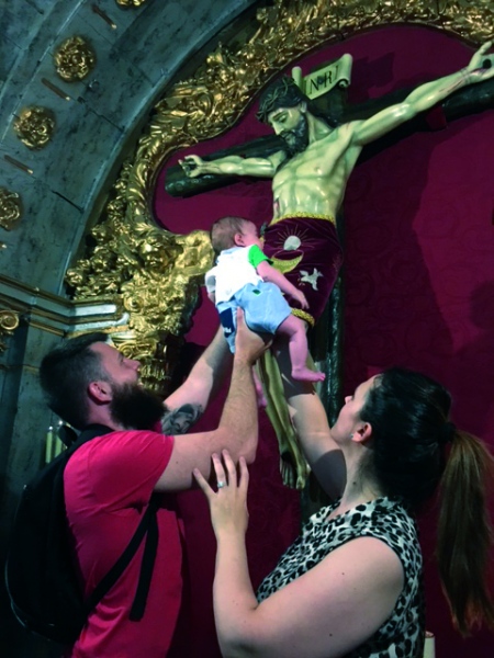 Dos fieles acercan a su hijo a la imagen del Cristo.